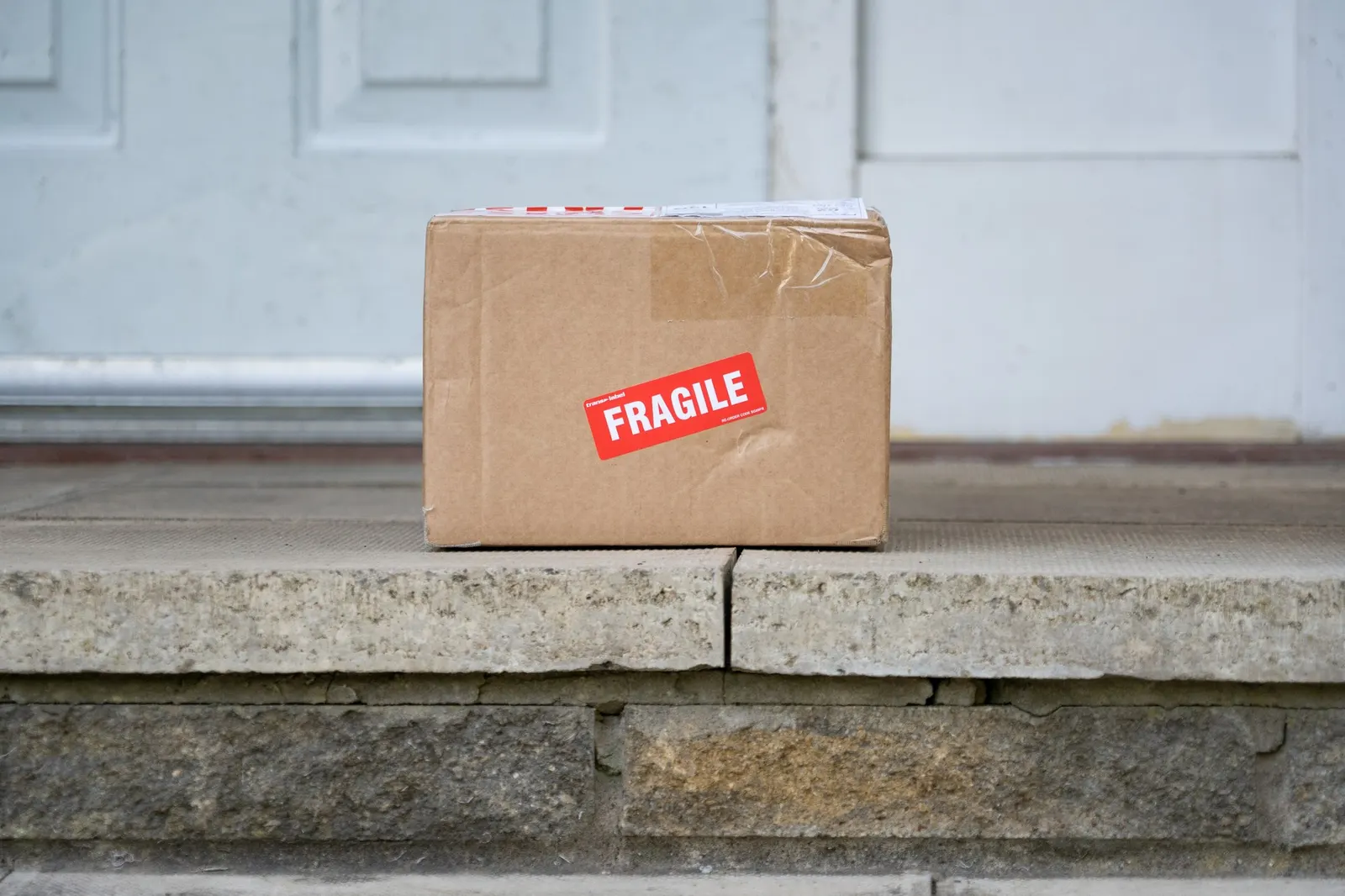 Картонная посылка с наклейкой Fragile у входной двери